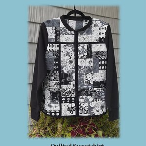 May include: A quilted sweatshirt jacket with a black and white floral patchwork design on the front and black sleeves. The jacket is hanging on a black hanger. The text "Charm Pack" and "Quilted Sweatshirt Jacket" are visible.