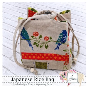 May include: A beige linen Japanese rice bag with a drawstring closure. The bag features a colorful patchwork design with birds, flowers, and polka dots. The bag has wooden beads on the drawstrings.
