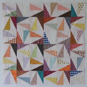 May include: A patchwork quilt square featuring a repeating pattern of colorful triangles. The triangles are made from various patterned fabrics in shades of pink, blue, yellow, orange, and brown, set against a neutral background.