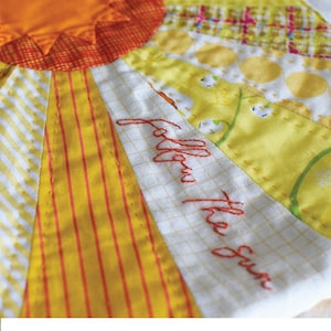 May include: A quilted pouch with a sun design and the text "Follow the Sun" in red embroidery. The pouch is made of yellow, orange, and white fabric. The text "Quippy Zippy Pouch" is printed in black at the bottom of the image. The text "By Jen Kingwell" and "Pattern and Acrylic Templates" are printed in black below the pouch.