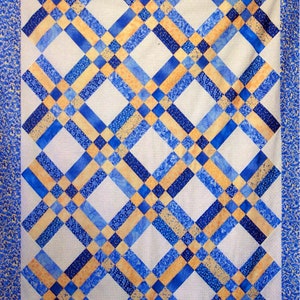 May include: A quilt with a diamond pattern in shades of blue and yellow. The quilt is made of fabric with a small, speckled pattern.