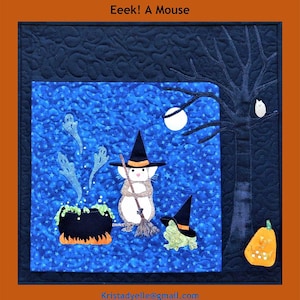 May include: A blue and black quilted wall hanging with a mouse wearing a witch's hat and holding a broom. The mouse is standing in front of a cauldron with green liquid and steam coming out of it. There are ghosts in the background and a full moon. The text "Eek! A Mouse" is at the top of the image.