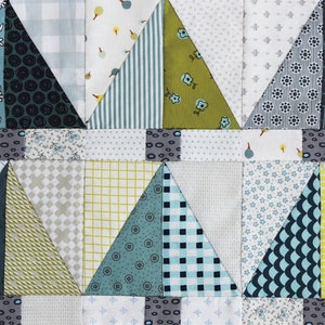 May include: A quilt block with a patchwork design featuring triangles in various shades of blue, green, and yellow. The triangles are arranged in a repeating pattern, creating a geometric design.