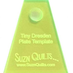 May include: A green plastic template for making tiny Dresden plates. The template has a circle in the center and the text "Tiny Dresden Plate Template" and "Suzn Quilts... www.SuznQuilts.com" printed on it.