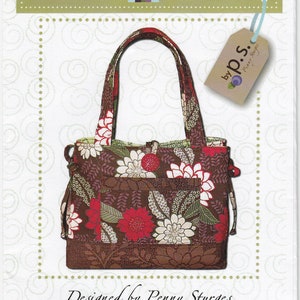 May include: A brown tote bag with a floral print featuring red, white, and green flowers. The bag has a brown leather handle and a small pocket on the front. The bag is labeled "ps008 Bow Tucks Tote" and "Designed by Penny Sturges".
