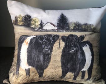 May include: A square throw pillow featuring a printed illustration of two black and white belted cows standing in a field. The background depicts a rural landscape with a white house, trees, and a stone wall under a soft, neutral sky.