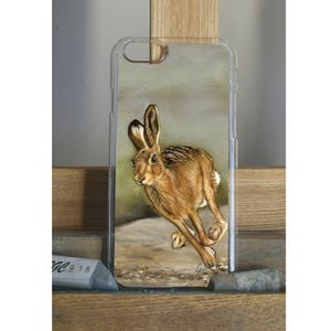 May include: A clear phone case featuring a brown and white illustration of a rabbit running through a field.