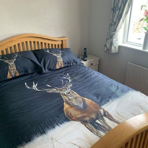 Puede incluir: Una estructura de cama de madera con una funda nórdica negra con un estampado de ciervo grande. La funda nórdica tiene dos fundas de almohada a juego con estampados de ciervo más pequeños.