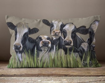 May include: A rectangular pillow with a beige linen fabric cover features a colorful painting of five black and white cows peeking out from a field of green grass.