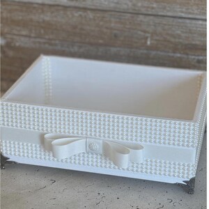 May include: A white rectangular decorative tray with pearl accents and a white ribbon bow. The tray has a pearl border and sits on four ornate metal feet. The interior of the tray is white.