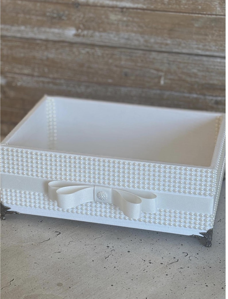 May include: A white rectangular decorative tray with pearl accents and a white ribbon bow. The tray has a pearl border and sits on four ornate metal feet. The interior of the tray is white.