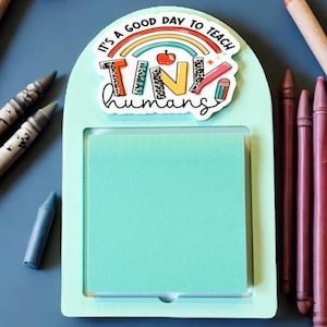 May include: A white and light blue memo board with a rainbow and the text "It's a good day to teach tiny humans". The memo board has a removable sticky note.