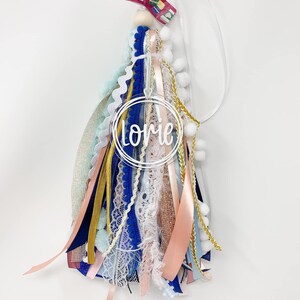 May include: A blue, pink, white, and gold tassel keychain with a clear circle charm that says "Lorie" in white lettering.