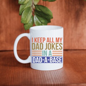 May include: White ceramic mug with a colorful graphic that reads "I keep all my dad jokes in a dad-a-base".