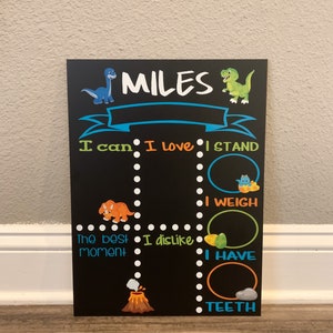 Puede incluir: Una pizarra negra con un tema de dinosaurio. Dice "MILES" en la parte superior y tiene una lista de indicaciones para que un ni&ntilde;o las complete, como "Puedo", "Me encanta", "Me pongo de pie", "Peso", "El mejor momento", "No me gusta", "Tengo" y "Dientes".