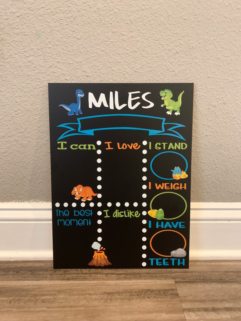 Puede incluir: Una pizarra negra con un tema de dinosaurio. Dice "MILES" en la parte superior y tiene una lista de indicaciones para que un ni&ntilde;o las complete, como "Puedo", "Me encanta", "Me pongo de pie", "Peso", "El mejor momento", "No me gusta", "Tengo" y "Dientes".