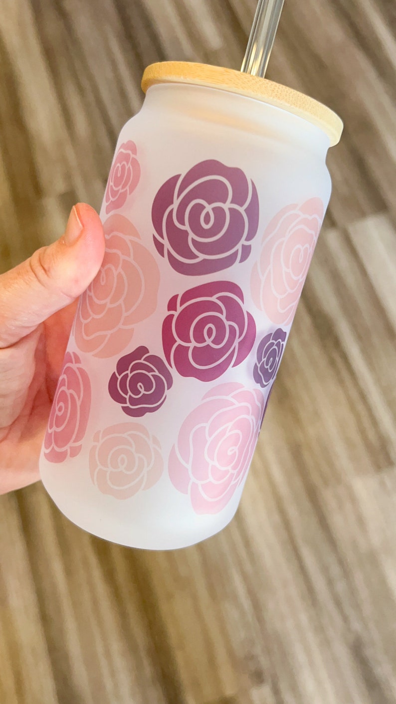 May include: A frosted glass reusable water bottle with a bamboo lid and a straw. The bottle has a pink and purple floral design.