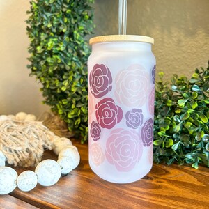 May include: A frosted glass tumbler with a bamboo lid and a clear glass straw. The tumbler has a pink and purple floral pattern.