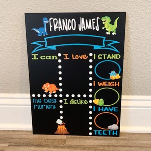 Puede incluir: Una pizarra negra con tem&aacute;tica de dinosaurios. Tiene el nombre "FRANCO JAMES" en la parte superior. La pizarra tiene secciones para "Puedo", "Me encanta", "Me pongo de pie", "El mejor momento", "No me gusta", "Peso", "Tengo" y "Dientes".
