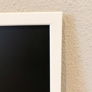 K&ouml;nnte beinhalten: Eine wei&szlig;e gerahmte Tafel mit einer schwarzen Oberfl&auml;che. Die Tafel h&auml;ngt an einer Wand.