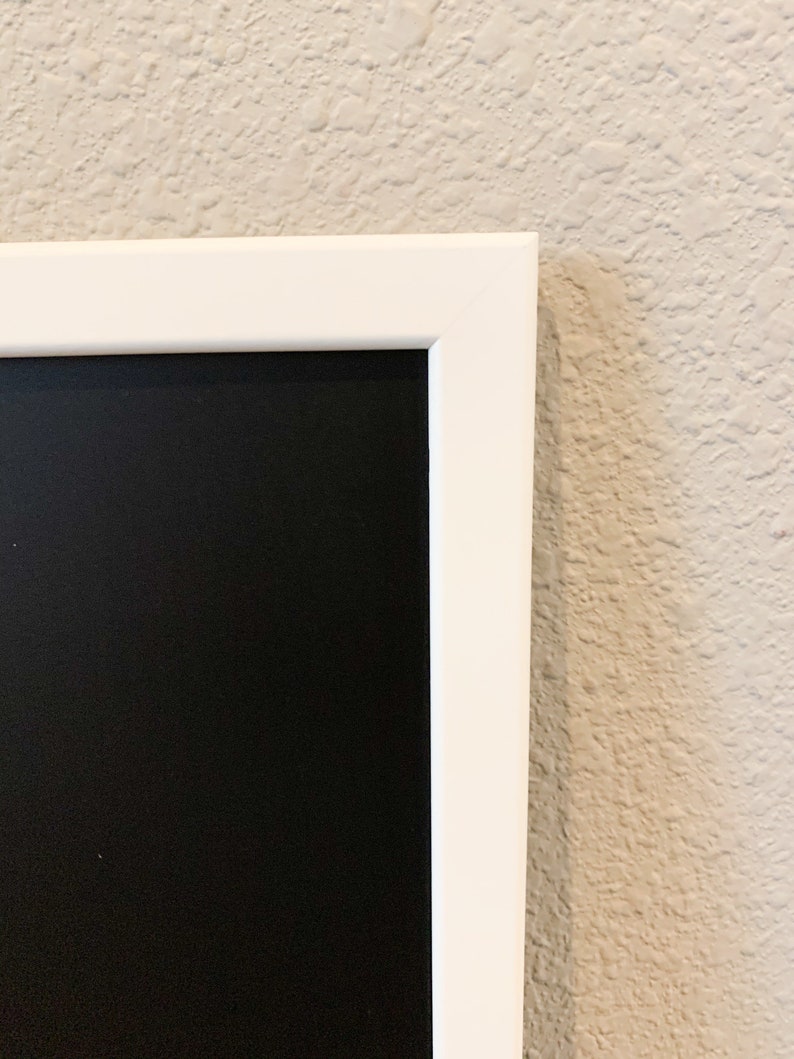 K&ouml;nnte beinhalten: Eine wei&szlig;e gerahmte Tafel mit einer schwarzen Oberfl&auml;che. Die Tafel h&auml;ngt an einer Wand.