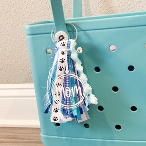 May include: A turquoise tote bag with a white and blue tassel keychain that says "MOM" in a circle. The keychain also has black paw prints on it.