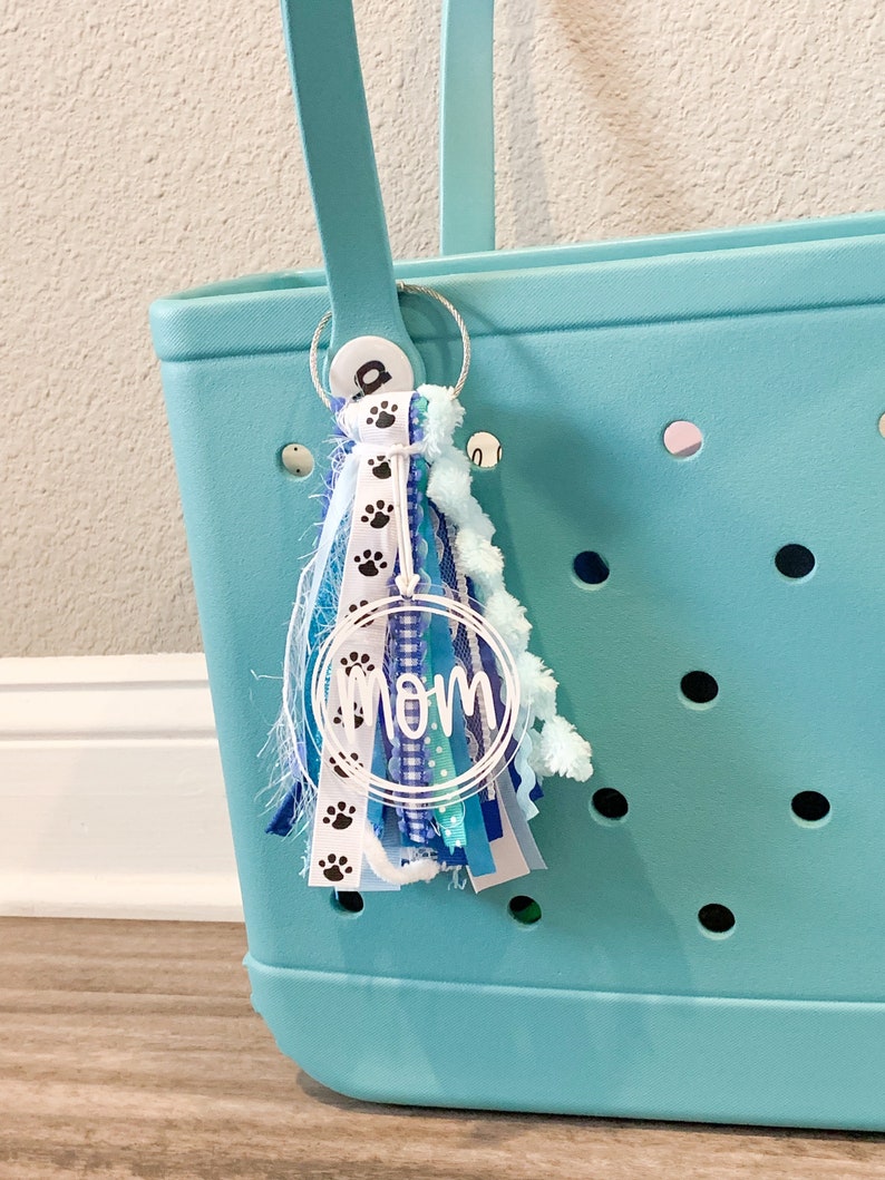 May include: A turquoise tote bag with a white and blue tassel keychain that says "MOM" in a circle. The keychain also has black paw prints on it.