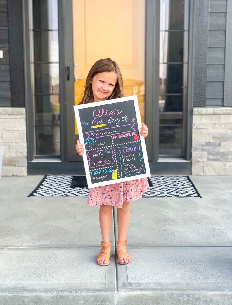 Shows child holding a milestone chalkboard sign that is reusable to document milestones for the first and last day of school.