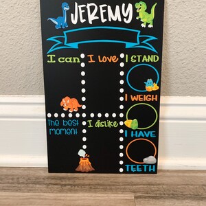Puede incluir: Una pizarra negra con tem&aacute;tica de dinosaurios. La pizarra tiene el nombre "JEREMY" en la parte superior. Tiene una pancarta azul con borde blanco. La pizarra tiene una lista de cosas que Jeremy puede hacer, incluyendo "Puedo", "Me encanta", "Me pongo de pie", "Peso", "El mejor momento", "No me gusta", "Tengo", y "Dientes".