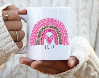 May include: White ceramic mug with a pink, brown, and leopard print rainbow design. The rainbow has a pink heart in the center and the word "LULU" written below it.