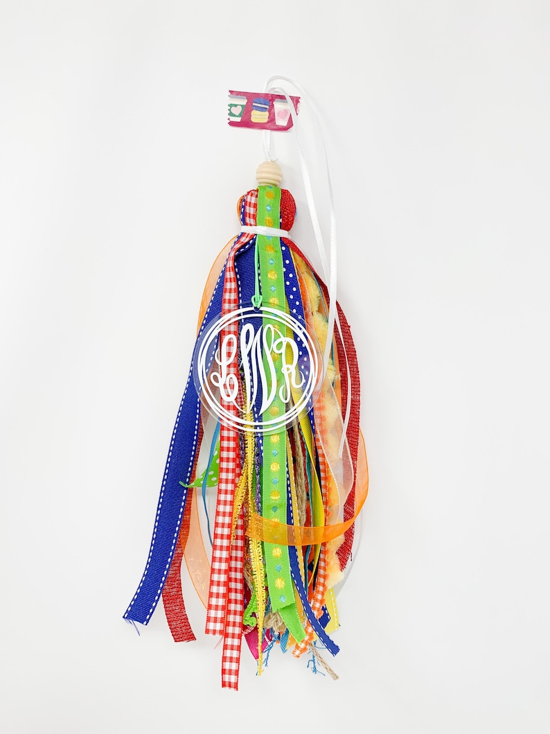 May include: A colorful tassel keychain with a white monogram "LSA" in a clear circle. The tassel is made of various ribbons in red, blue, green, yellow, and orange.