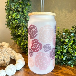 May include: A frosted glass tumbler with a bamboo lid and a glass straw. The tumbler has a floral pattern with pink, red, and purple roses.