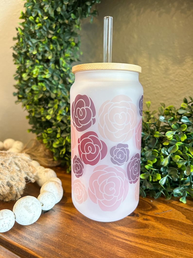 May include: A frosted glass tumbler with a bamboo lid and a glass straw. The tumbler has a floral pattern with pink, red, and purple roses.