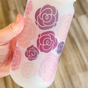 May include: A frosted glass tumbler with a bamboo lid and a clear drinking straw. The tumbler has a pink and purple floral pattern.