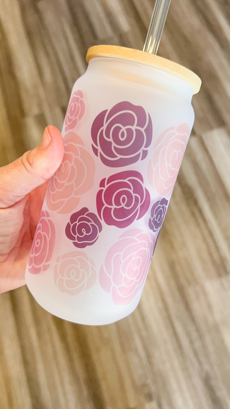 May include: A frosted glass tumbler with a bamboo lid and a clear drinking straw. The tumbler has a pink and purple floral pattern.