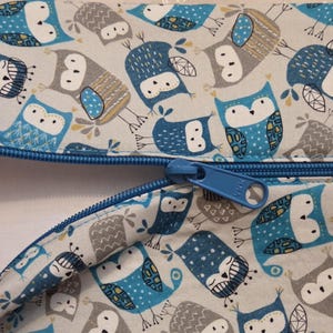 May include: Two zippered pouches with a repeating pattern of blue and gray owls on a light background. The zippers are blue, and the pouches are made of fabric. The owl design includes various patterns and details.