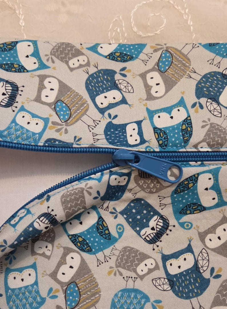 May include: Two zippered pouches with a repeating pattern of blue and gray owls on a light background. The zippers are blue, and the pouches are made of fabric. The owl design includes various patterns and details.