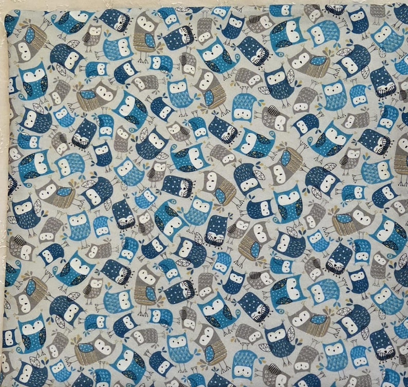 May include: A fabric with a repeating pattern of owls in shades of blue, gray, and brown on a light gray background. The owls have various designs and expressions, creating a whimsical and decorative textile.