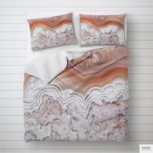 May include: A bedding set featuring a detailed agate stone pattern in shades of orange, brown, and white. The set includes a duvet cover and two pillowcases, all with a layered, naturalistic design. The bedding is displayed on a white surface.