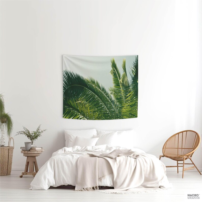 a bedroom with a large tapestry hanging on the wall depicting lush green palm leaves. The room has a white color scheme, with a bed, a chair, and a potted plant.