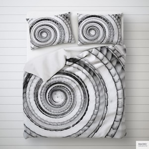 Könnte beinhalten: Bettwäsche-Set mit einem Spiralmuster in Schwarz-Weiß. Das Set besteht aus einem Bettbezug und zwei Kissenbezügen. Das Design zeigt konzentrische Kreise in Grau- und Weißtönen. Die Bettwäsche liegt auf einer weißen Oberfläche.