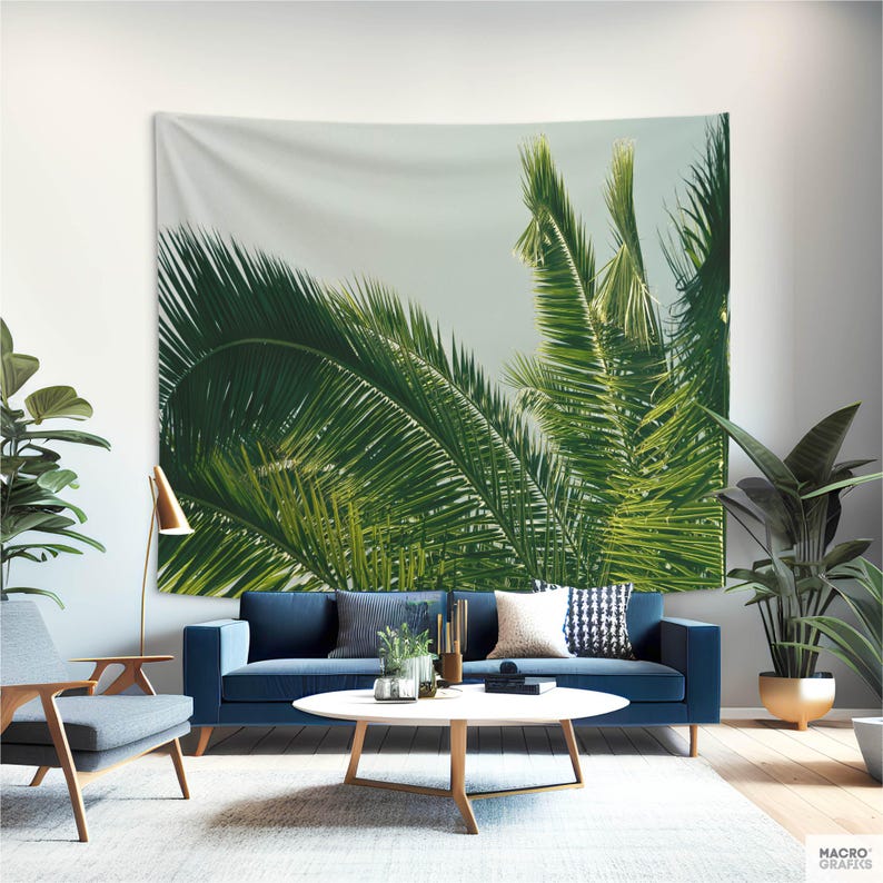 a living room with a large tapestry of palm leaves hanging on the wall, creating a tropical ambiance. The room is furnished with a blue sofa, a wooden coffee table, and a gray armchair. The space is decorated with various plants, including a large potted plant and a smaller potted plant, adding a touch of greenery to the room.