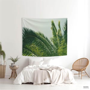 a bedroom with a large tapestry of palm leaves hanging on the wall above a bed. The tapestry is predominantly green and white, creating a tropical ambiance in the room.