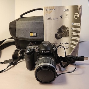 May include: A black Fujifilm FinePix S5200 digital camera with a lens cap, a black Case Logic camera bag with a shoulder strap, a USB cable, and a printed instruction manual featuring the camera model name and Fujifilm branding.