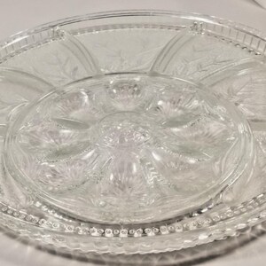 May include: Clear glass serving dish with a central, circular compartment and several surrounding sections. The dish features a decorative leaf pattern and a beaded edge, suitable for serving appetizers or snacks.