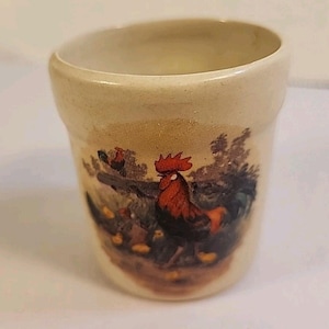 May include: A white ceramic mug with a black handle and the text "But First, Coffee" in a bold, black font. The mug is set against a blurred background, suggesting a cozy setting.