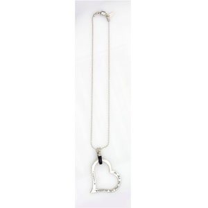 May include: Silver-toned necklace featuring a large, open heart pendant. The heart has an inscription and hangs from a delicate chain. The necklace is displayed against a white background, highlighting its design and details.