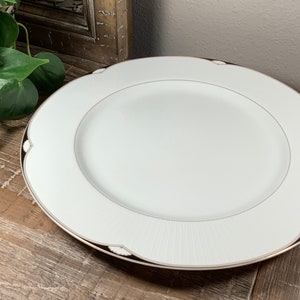 May include: White ceramic dinner plate with a black and gold rim. The plate has a subtle embossed design.