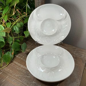 May include: Two white ceramic serving platters with a central dip bowl and two outer sections. The platters have a leaf pattern and are displayed on a wooden surface. The platters are approximately 10 inches in diameter.