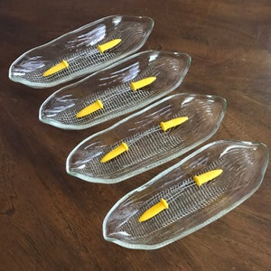 May include: Set of four clear glass corn on the cob serving dishes with yellow plastic corn kernels.